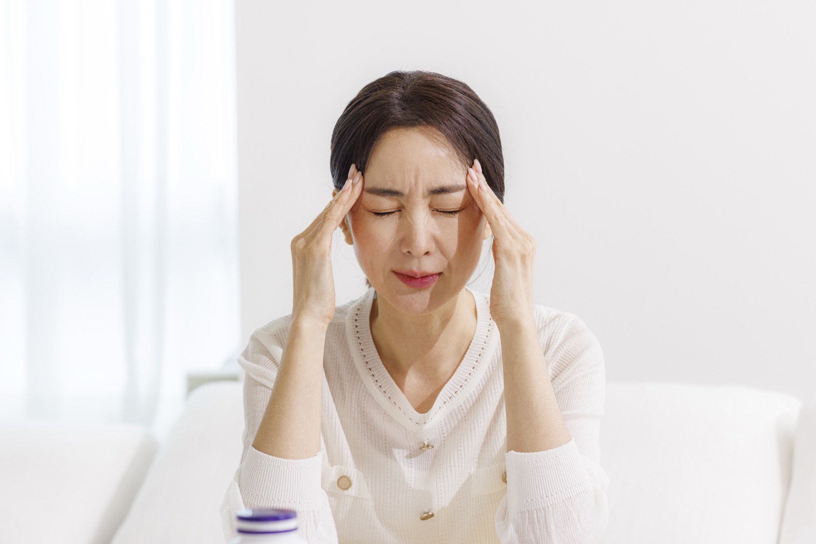 감기 몸살로 두통을 느껴 관자놀이를 짚고 있는 여성